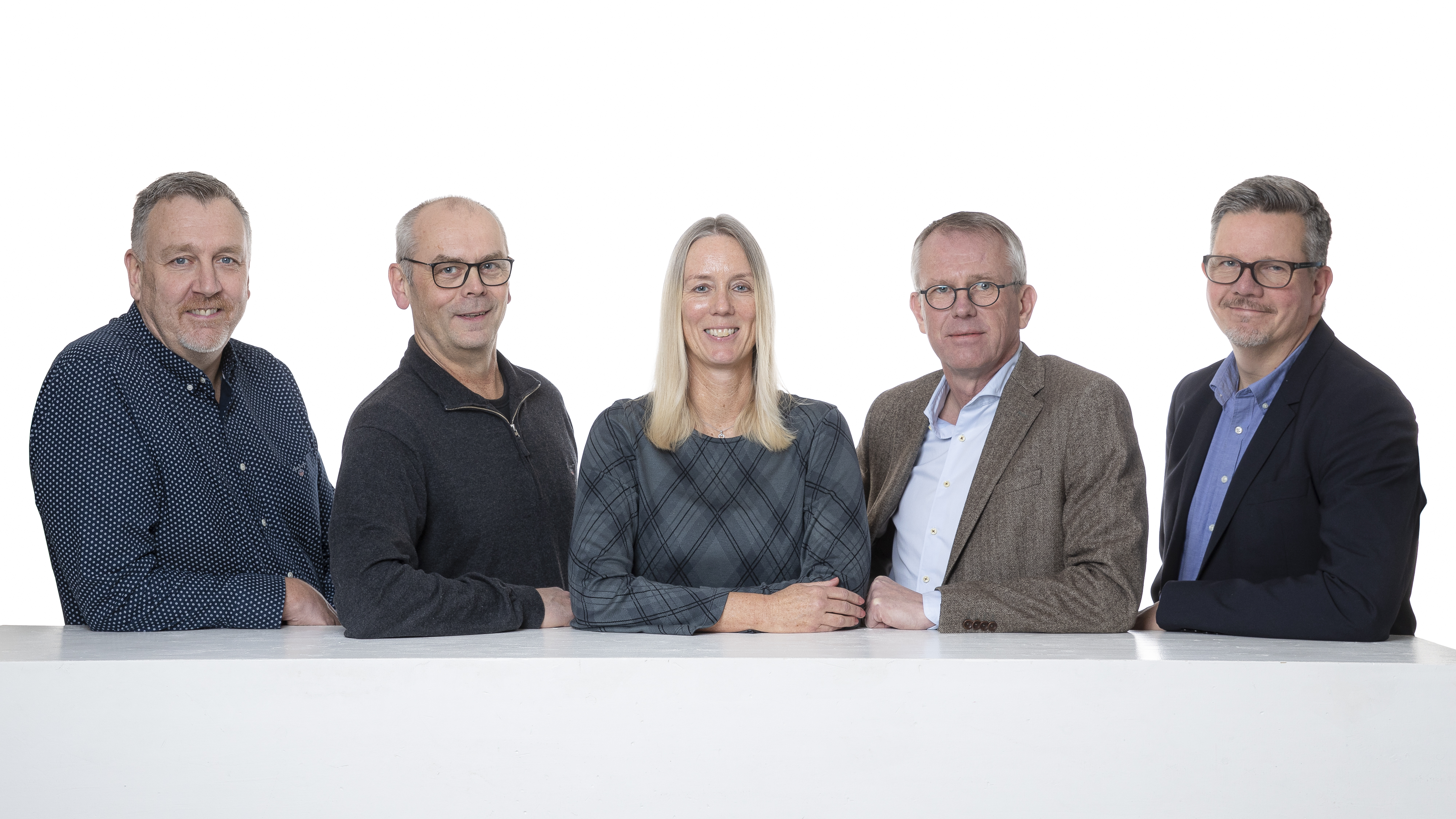 Gruppfoto av sex personer, tre stående och tre sittande, mot en vit bakgrund. Fyra män och två kvinnor är formellt klädda, med neutrala uttryck och avslappnad hållning.